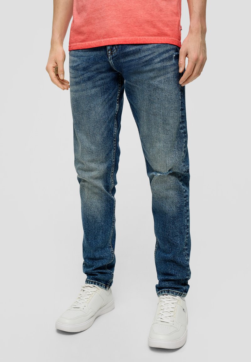 Jeans de mezclilla azul claro con corte slim, con detalles de desgaste y arrugas. Combinados con zapatillas blancas de corte bajo.