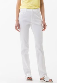 Vita raka jeans med framfickor, knappstängning och bälteshällor, i kombination med sandaler med silverdetaljer och en gul topp.