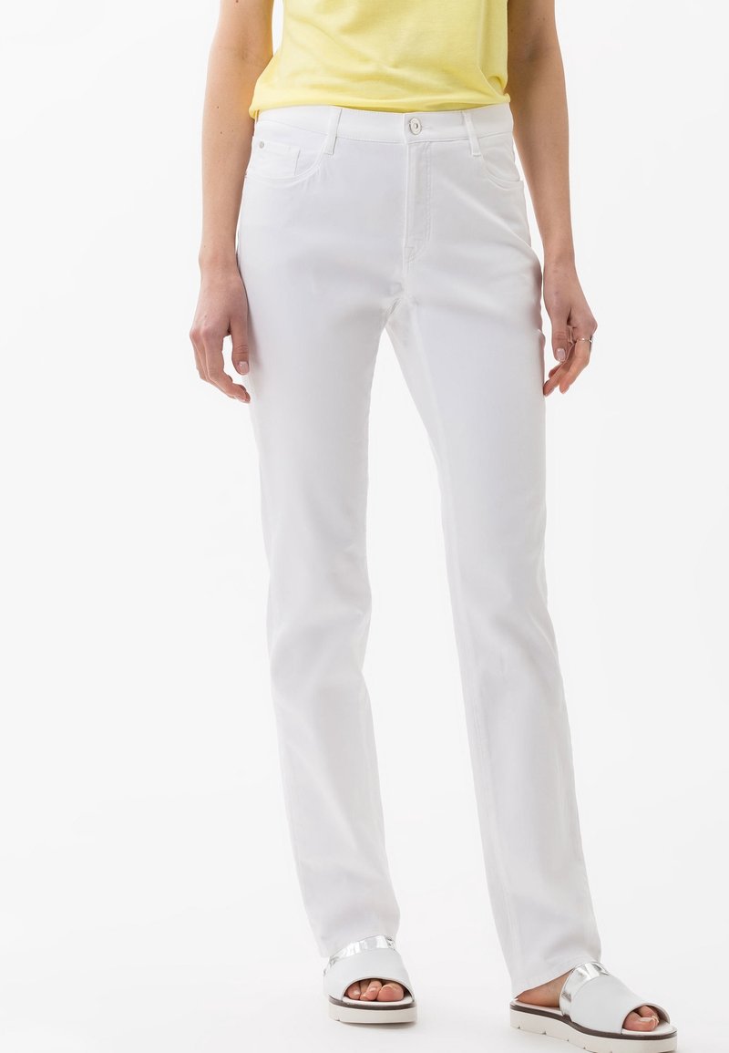 Vita raka jeans med framfickor, knappstängning och bälteshällor, i kombination med sandaler med silverdetaljer och en gul topp.