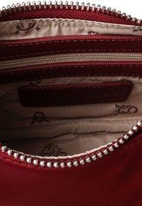 Rød stofpung med lynlåslukning, der har flere rum og en glat satinfôr. Sølvhardware langs lynlåsen.