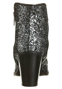 Bottine noire avec un talon épais, recouverte de paillettes argentées, montrée de l'arrière, mettant en valeur la texture et la forme du talon.