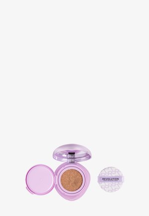 Poudre compacte violette avec fond de teint cushion à l’intérieur et un applicateur en éponge ronde imprimé "Revolution" à côté, sur fond blanc.