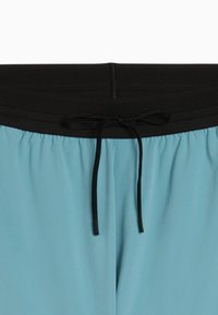 Ανοιχτό μπλε σορτς με φαρδύ μαύρο ελαστικό ζωνάρι και μαύρο κορδόνι δεμένο σε φιόγκο στο κέντρο μπροστά.