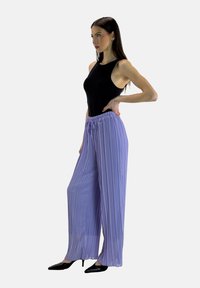 Hellviolette, plissierte Hosen mit weitem Bein, elastischem Bund und Kordelzug. Kombiniert mit einem schwarzen ärmellosen Oberteil und schwarzen spitzen High Heels.