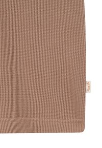 Gros plan sur un tissu tricoté côtelé marron clair avec une petite étiquette beige cousue sur le bord droit.