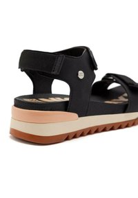 Sandal negra con correas ajustables, una plantilla texturizada y una suela estratificada con acentos en blanco y marrón claro.