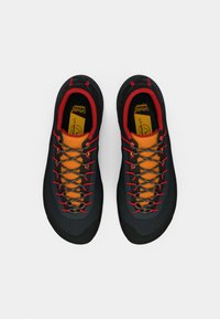 Melni pārgājienu apavi ar strukturētu virsējo daļu, spilgti oranžu auklu un sarkaniem akcentiem. Iezīmējas ar izturīgu zoli un atbalstošu potītes dizainu.