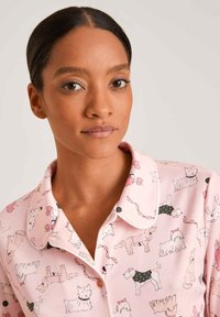 Rosa Schlafanzugshirt mit Hundillustrationen. Verfügt über einen Kragen, Knopfdetails und verspielte Muster verschiedener Hunde in unterschiedlichen Posen und Outfits.