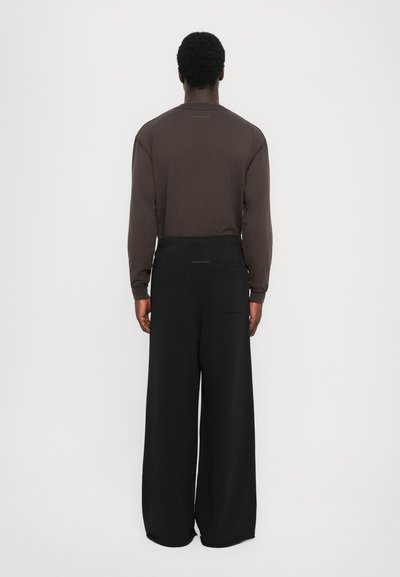 Long-sleeve brown shirt with a crew neck, paired with loose black trousers featuring a back pocket and elastic waistband.