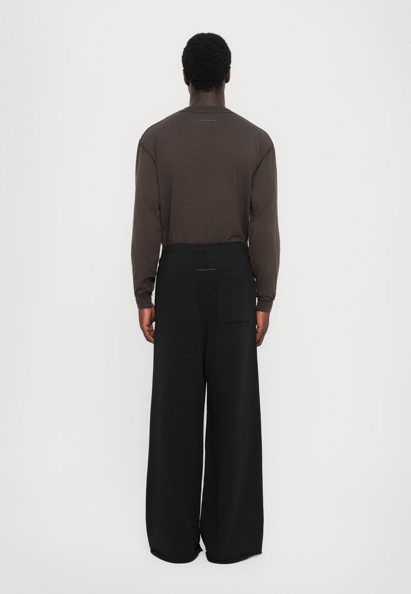 Langsleeve bruine shirt met een ronde hals, gecombineerd met losse zwarte broek met een achterzak en elastische tailleband.