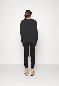 Felpa nera con maniche lunghe, vestibilità comoda, polsini e orlo a costine. Abbinata a leggings neri e scarpe slip-on beige. Design semplice.