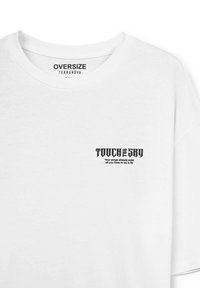 T-shirt bianca oversize in cotone. Presenta una stampa grafica scura sul lato sinistro del petto con testo. Collo rotondo e maniche corte.