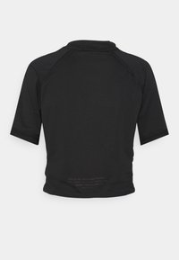 Kortärmad svart skjorta med hög hals, har en texturerad tyg, raglanärmar och en tryckt etikett vid fållen.