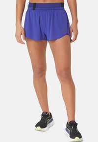 Violetit urheilushortsit, joissa on teksturoitu kuosi, joustava vyötärönauha ja pieni tasku. Yhdistetty mustiin ja violetteihin juoksukenkiin.