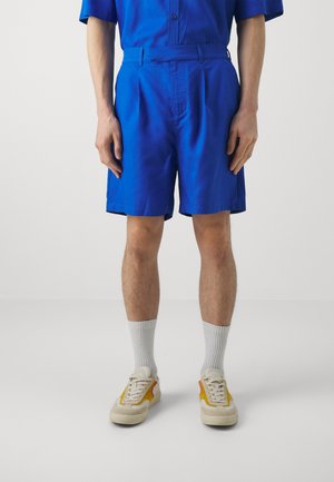 Blauwe shorts van lichtgewicht stof, met een vlakke voorkant, zijzakken en een gladde afwerking, gecombineerd met beige sneakers en grijze sokken.