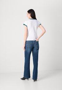White t-shirt with green trim, paired with blue wide-leg jeans and black heeled boots. The t-shirt features a classic cut and short sleeves.