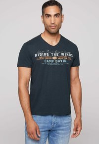 Marinblå v-ringad t-shirt med vit och orange grafisk text med utomhusteman. Kort ärm, avslappnad passform, mjukt bomullsmaterial.