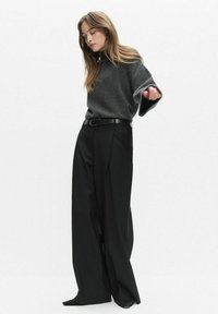 Szary, przeszły sweter z szerokimi rękawami, połączony z luźnymi czarnymi spodniami o wysokim stanie, zabezpieczonymi czarnym paskiem. Prosty design, bez wzorów.