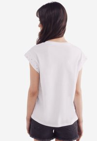 Hvid bomulds t-shirt med korte ærmer med små øjehuller, rund halsudskæring og en løs pasform, parret med sorte shorts.