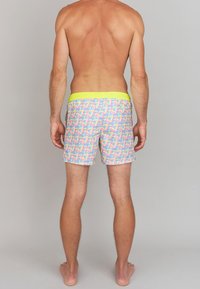 Shorts de bain avec un motif géométrique coloré incluant du rose, du bleu et du jaune, une taille élastique et une coupe au milieu de la cuisse. Vue arrière présentée.