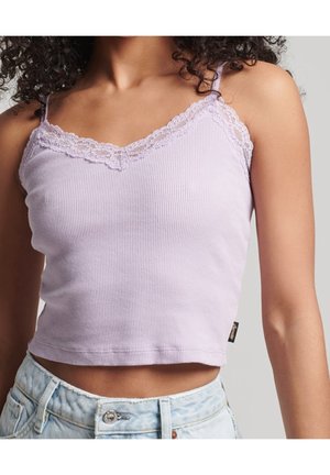 Woman wearing light purple ribbed crop top with lace trim and light blue high-waisted jeans, shown from neck to waist against gray background.