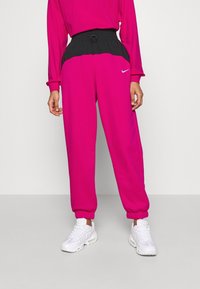 Rosa joggers med svart elastisk midja, manschetterade anklar och en liten vit logotyp på vänstra låret. Tillverkade av mjukt, hållbart tyg.