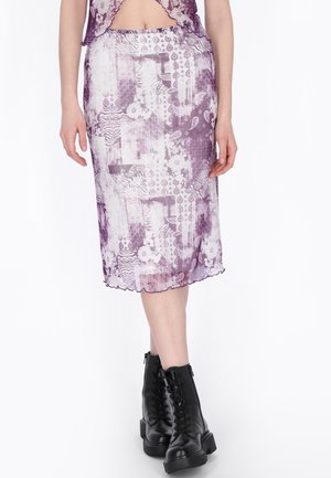 Donna che indossa una gonna midi viola con motivo a fantasia e un top corto, abbinati a stivali neri alla caviglia con lacci, su sfondo bianco.