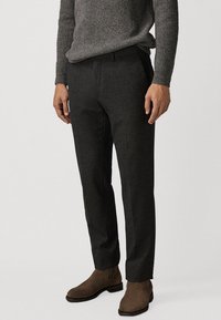 Donkergrijze op maat gemaakte broeken met een gladde textuur, slim fit en een geperste voorkant. Gecombineerd met een geribbeld grijs sweater en bruine laarzen.