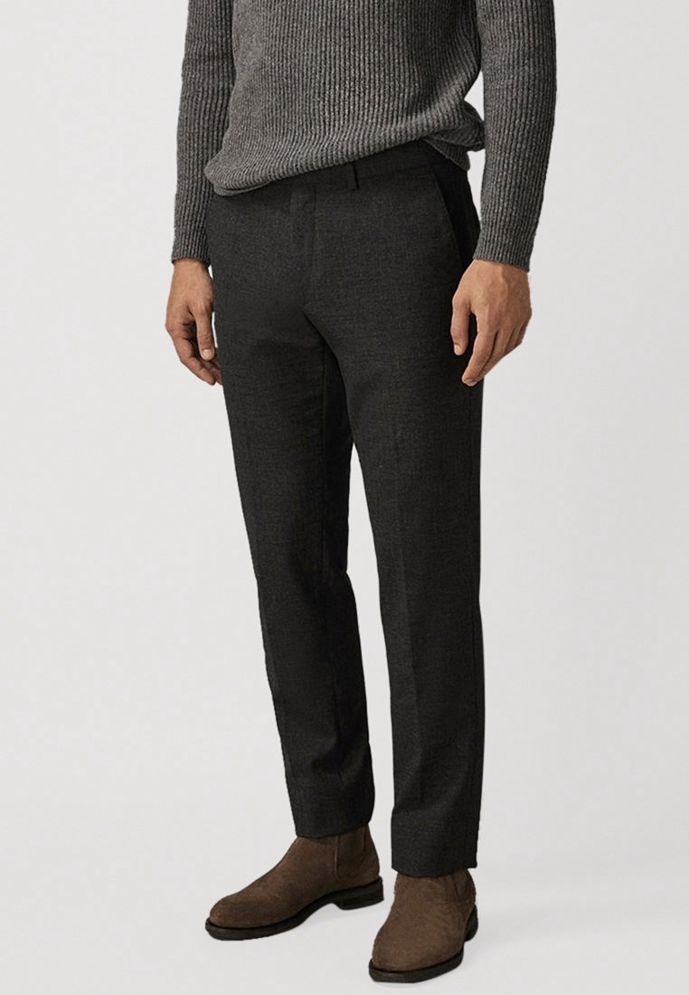 Donkergrijze op maat gemaakte broeken met een gladde textuur, slim fit en een geperste voorkant. Gecombineerd met een geribbeld grijs sweater en bruine laarzen.