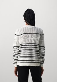 White knitted sweater with black striped patterns and diamond accents. Features a ribbed neckline and cuffs. Loose-fitting design.