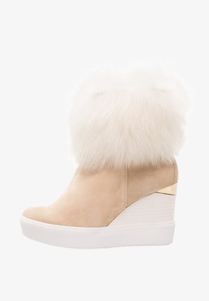 Bottine beige compensée avec large bordure en fourrure blanche épaisse et accent doré sur le talon, dotée d'une semelle en caoutchouc blanche.