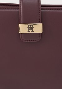 Burgundy színű kézitáska textúrázott bőrből, aranyszínű logózárral. Simább felület és tónusos varrási részletek jellemzik.