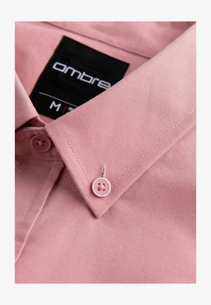 Nahaufnahme eines rosa Hemdkragens mit passendem Knopf und schwarzem Markenetikett mit der Aufschrift "ombre" und Größe M.