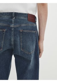 Tummansininen farkkushortsit, jossa on haalistunut pinta, ruskea nahkapaikka vyötäröllä ja kaksi takataskua, jotka on kirjottu kontrastivärillä.