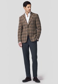 Brązowa marynarka w kratę z wykładanymi klapami, dwoma guzikami i dwoma kieszeniami, zestawiona z ciemnoszarymi, dopasowanymi spodniami i brązowymi skórzanymi butami.