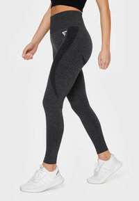 High-waisted black leggings with a heathered texture, featuring side panels and a small white logo. Paired with white athletic shoes.