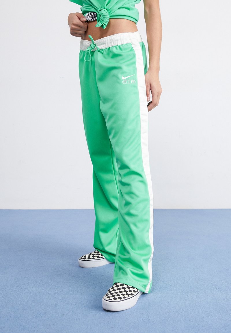 Green athletic pants made of smooth fabric with white side stripes and a drawstring waist, paired with black and white checkered shoes.
