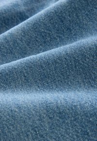 Țesătură de denim într-o nuanță albastru mediu, având o țesătură fină, texturată, cu o suprafață netedă și detalii de cusătură subtile.