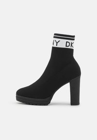 Černé kotníkové boty s pleteným svrškem, vysokým podpatkem a gumovou podrážkou. Má bílý značkový pruh na vrchu. Elegantní a přiléhavý design.