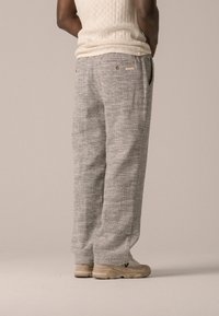 Pantalons gris clair à motifs en tissu texturé, avec une coupe décontractée et des poches, associés à des baskets beiges.