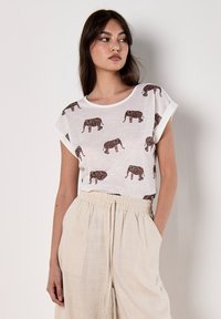 Camiseta blanca de manga corta con un estampado de elefantes en tonos rojo oscuro y negro, combinada con pantalones sueltos de color beige claro.