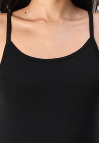 Débardeur noir à fines bretelles, en tissu lisse et extensible. Il présente une encolure arrondie et une coupe ajustée.