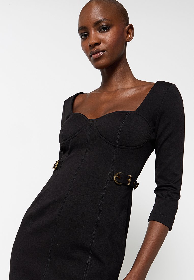 Zwarte aansluitende jurk met een vierkante halslijn, driekwart mouwen, accenten van gouden hardware en gedetailleerde structuur in het lijfje. Gladde textuur.