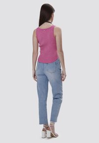 Top aderente rosa a costine con scollatura rotonda, abbinato a jeans azzurri e sandali bianchi con tacco quadrato. Vista posteriore.