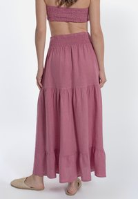 Gonna maxi a strati di colore rosa realizzata in tessuto leggero con vita elastica. Presenta un orlo arricciato ed è abbinata a sandali senza tacco intrecciati.