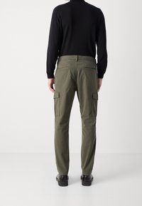 Olivově zelené cargo kalhoty s volným střihem, obsahující více kapes, hladkou texturou a kombinované s černými botami, viděné zepředu.