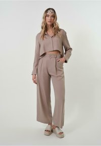 Blouse beige à coupe courte, pantalons beige taille haute avec plis, et sandales à plateforme légères. Tissu lisse, coupe décontractée, design minimal.