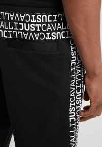 Black jogger pants featuring a white printed logo on the side, elastic waistband, and a back pocket with a smooth texture.
