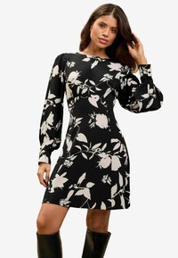 Rochie scurtă neagră cu modele florale albe, mâneci lungi și puffate, decolteu modest și corset ajustat. Material neted cu o ușoară strălucire.
