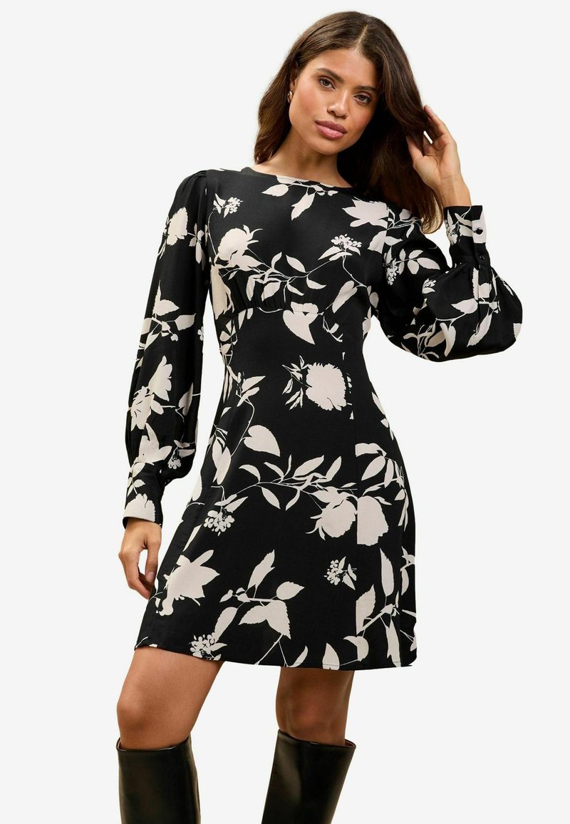 Rochie scurtă neagră cu modele florale albe, mâneci lungi și puffate, decolteu modest și corset ajustat. Material neted cu o ușoară strălucire.